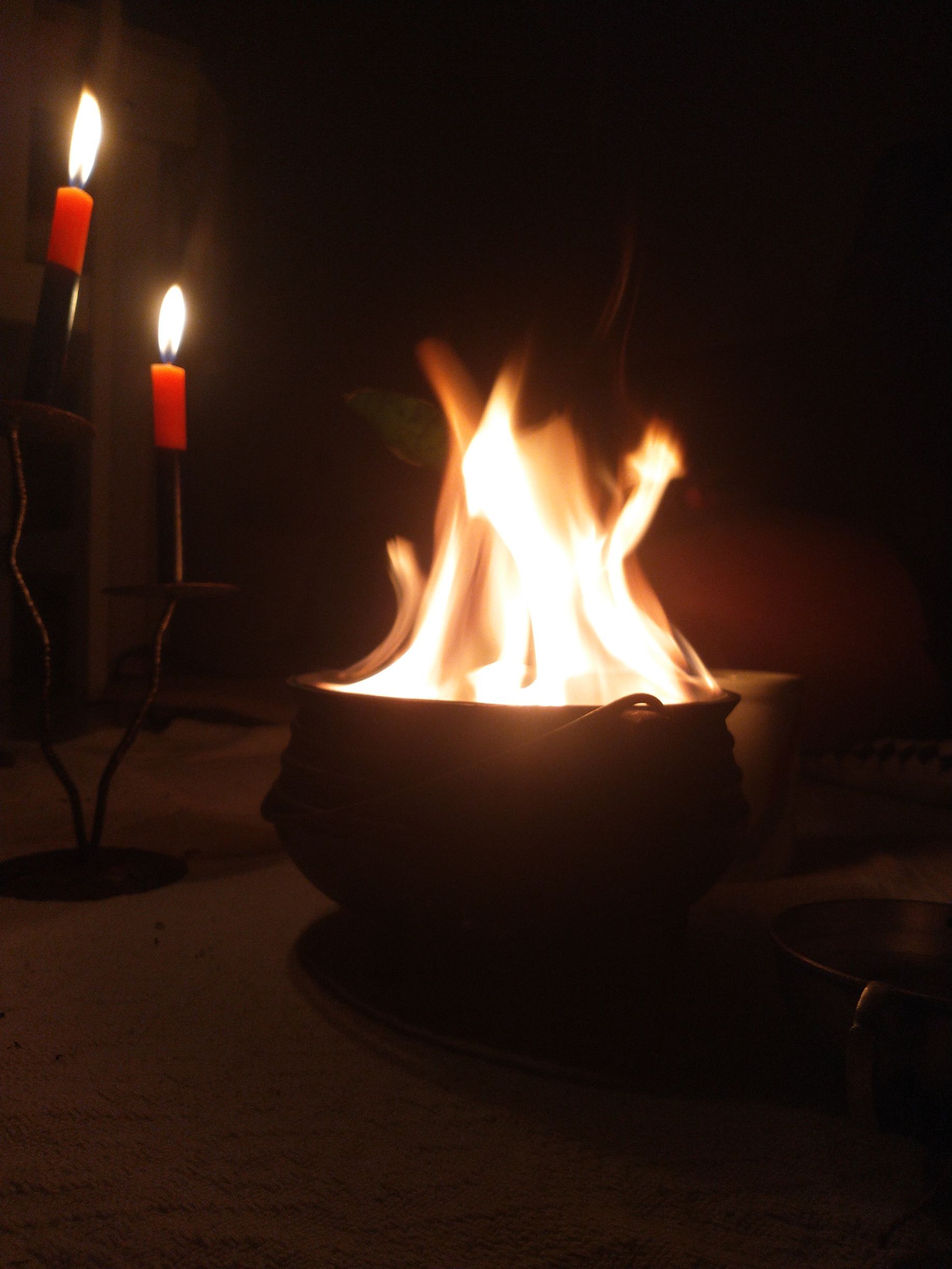 Cena à luz de velas. Uma tigela de fogo, com duas velas vermelhas acesas em um suporte de metal à esquerda.