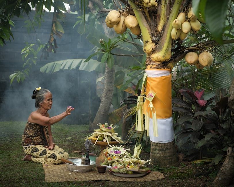 Mulher em traje tradicional oferecendo orações com oferendas perto de um coqueiro em um jardim.
