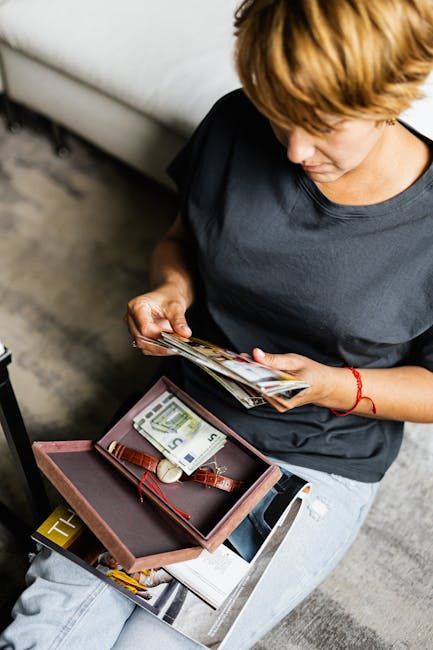 Mulher contando dinheiro, ao lado de um relógio e uma caixa. Camisa cinza, pulseira vermelha, cenário interno.
