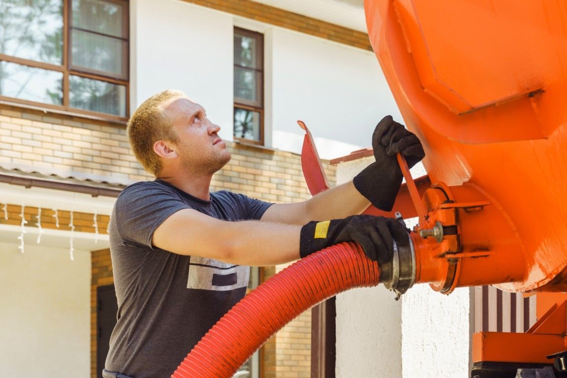 Man in gloves connecting red hose to an orange tank outside a house.