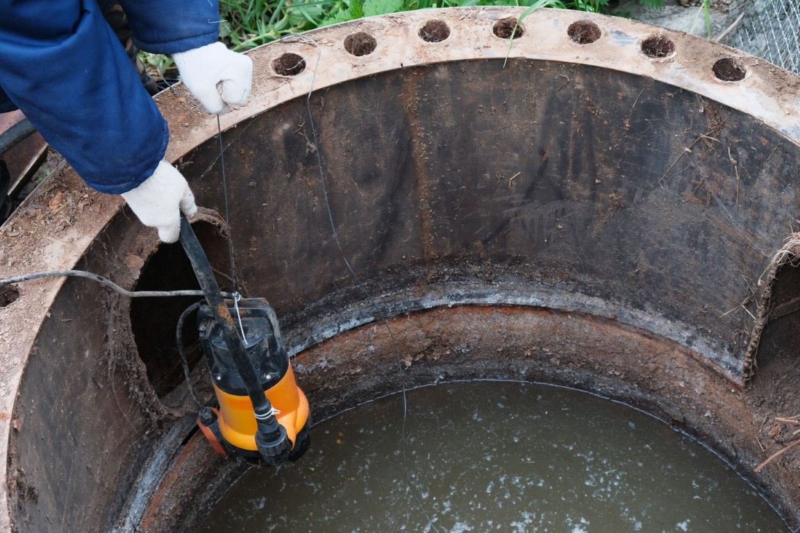 Person in white gloves using a pump to remove water from a rusty, circular industrial structure.