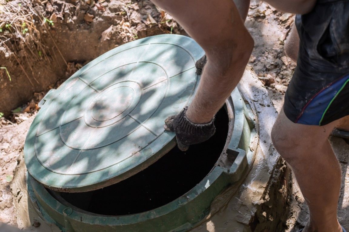 Person opening a green septic tank cover in an outdoor setting.