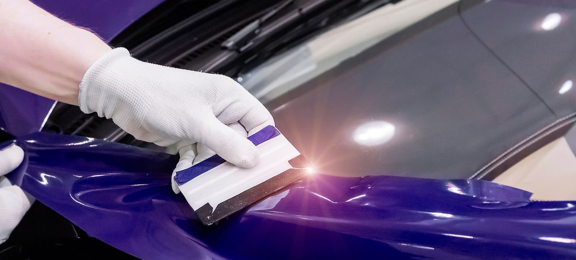 Person wearing gloves using a squeegee on a blue car surface.