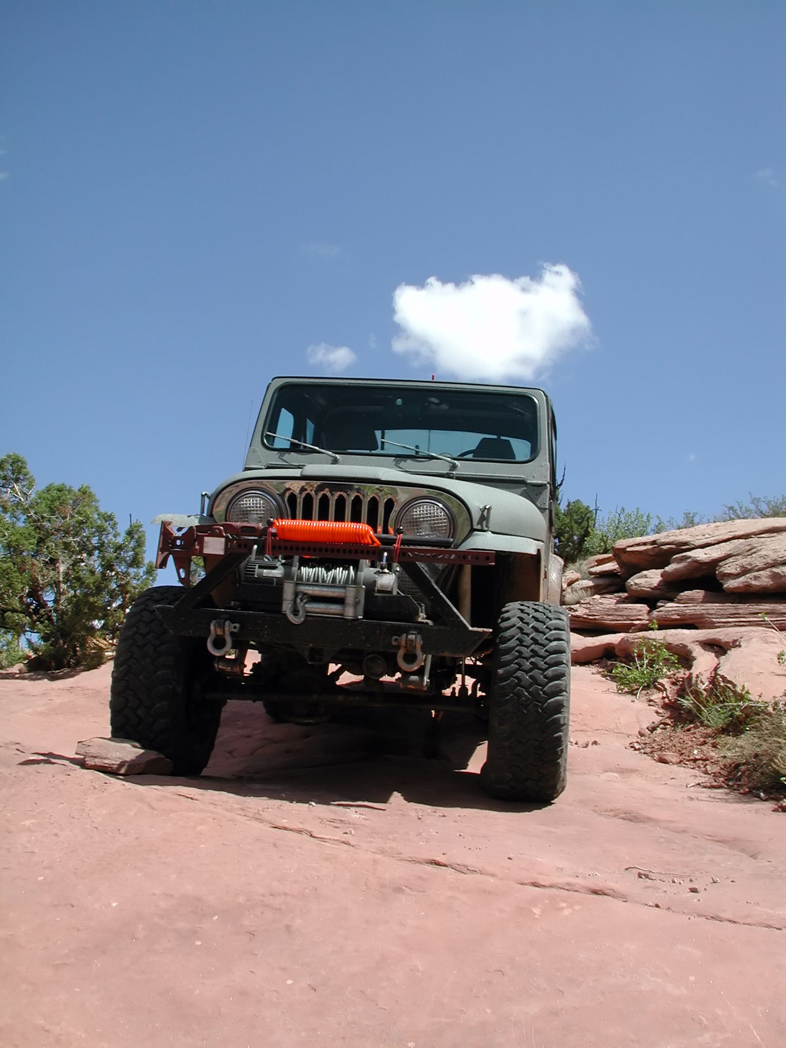 Gray Jeep Wrangler on a red rock trail under a blue sky with a cloud.
