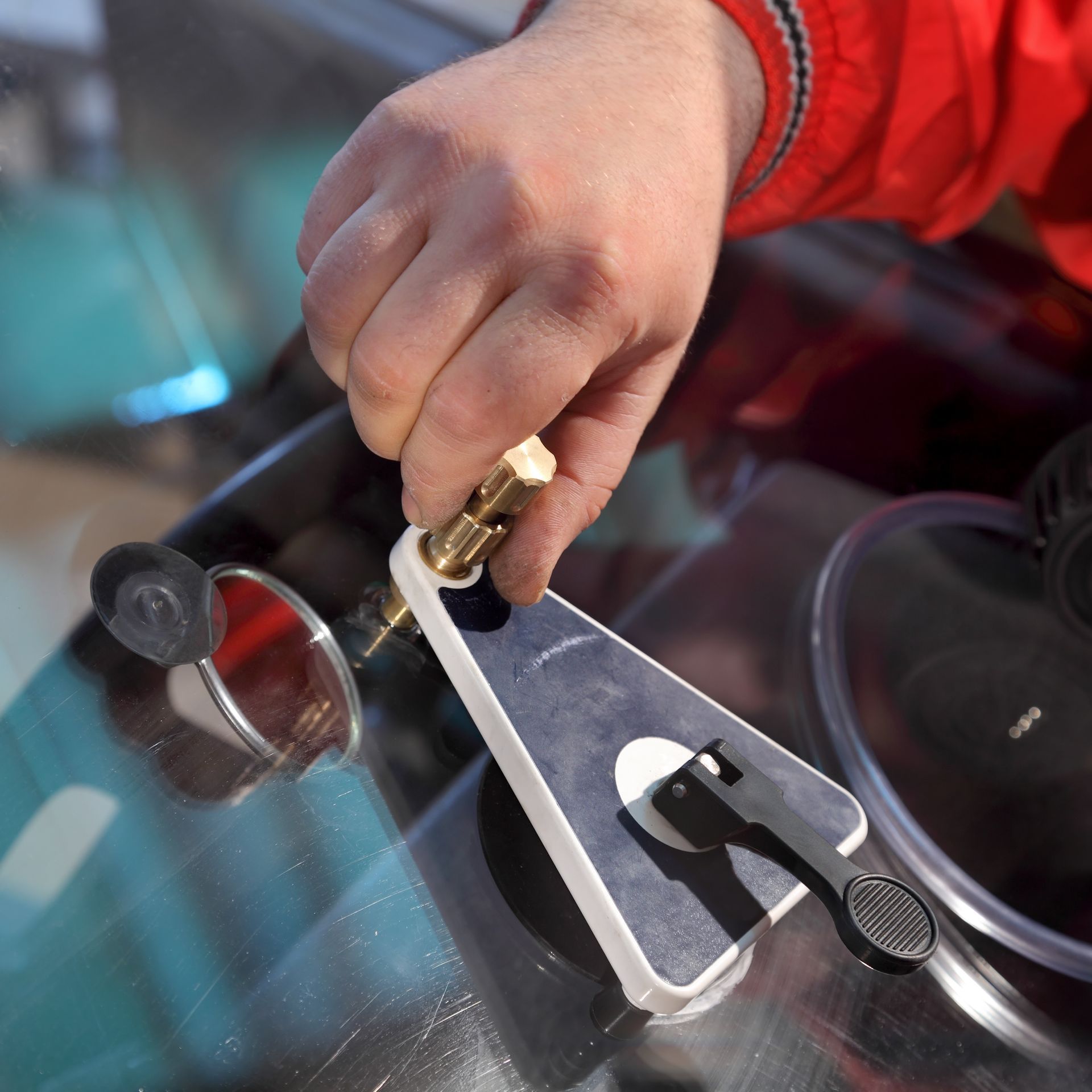 Hand using a windshield repair tool on a car windshield, fixing a crack.