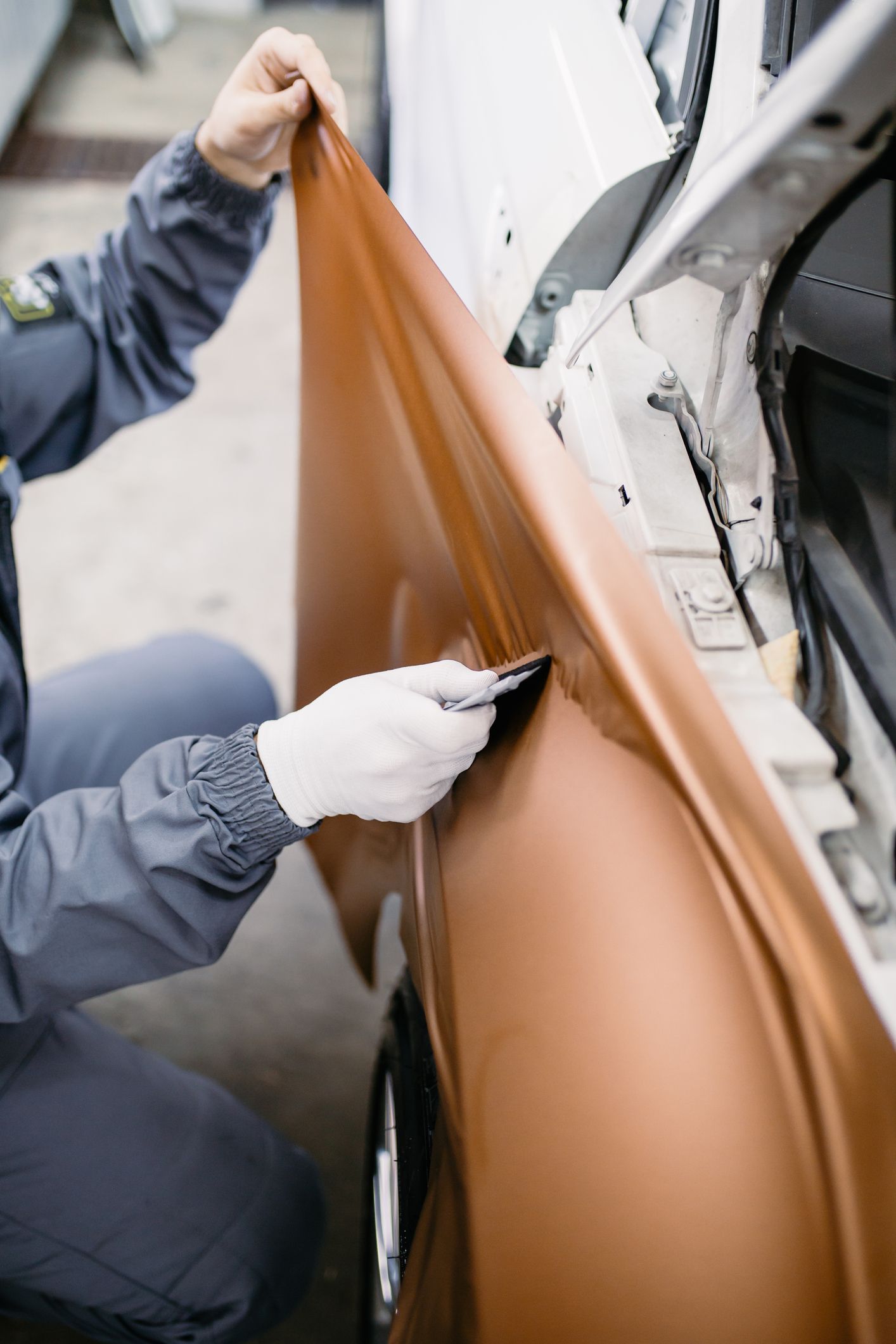 Person wrapping a car door with brown vinyl; using a blade to trim edges.