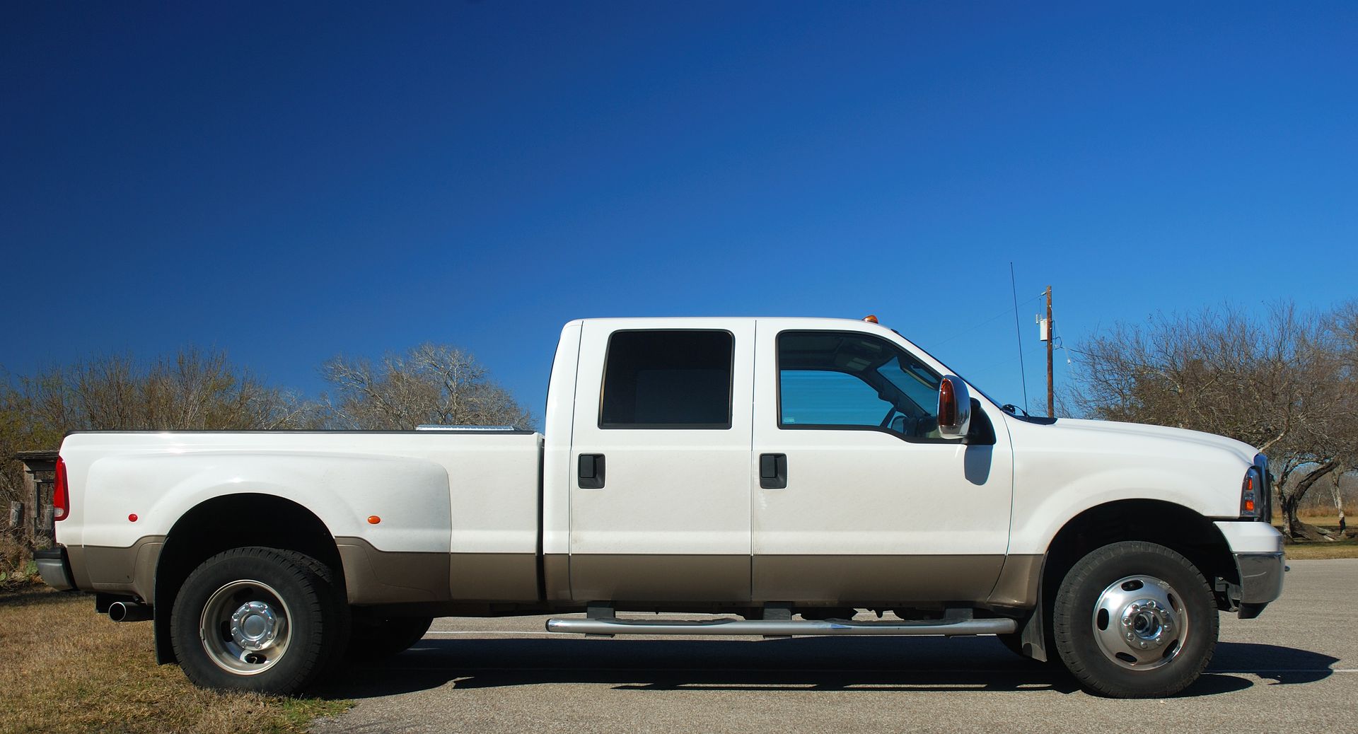 White and tan pickup truck on a road against a clear blue sky.