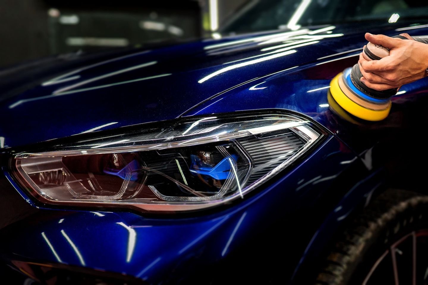 A person is polishing a blue car with a polisher.