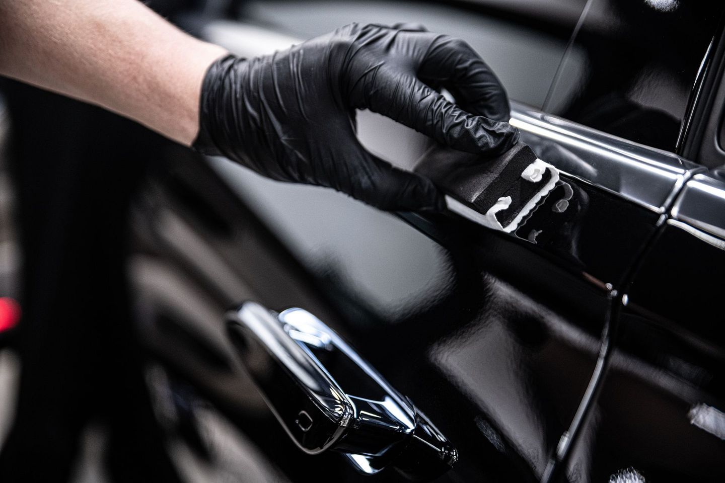 A person wearing black gloves is opening a car door.