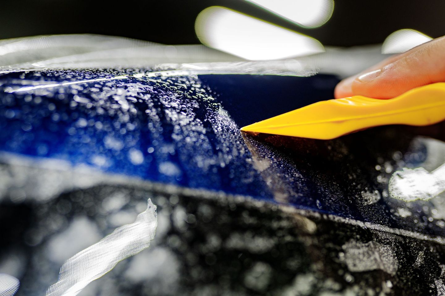 A person is cleaning a car with a yellow spatula.