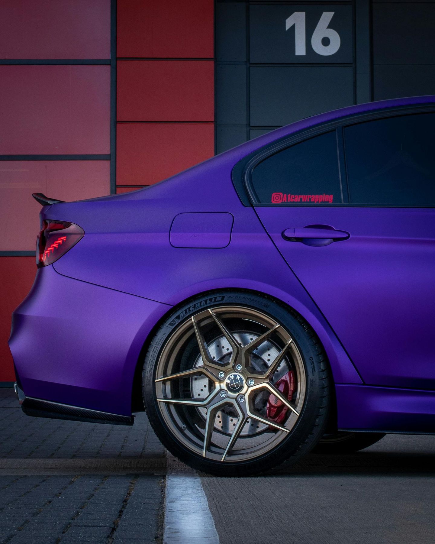 A purple car is parked in front of a building with the number 16 on it