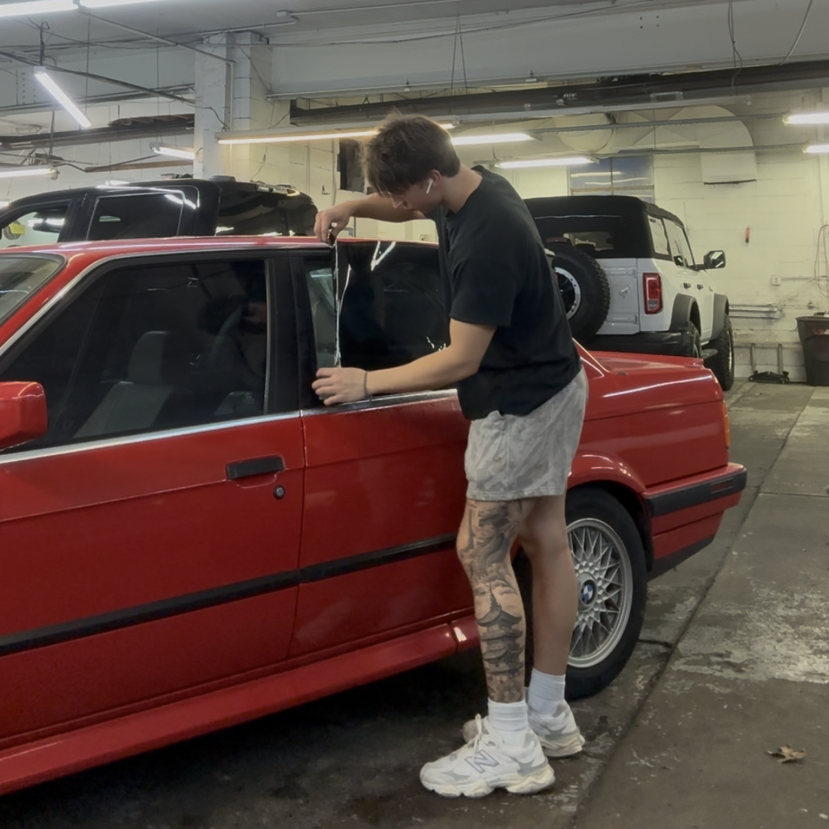 A man is standing next to a red car in a garage