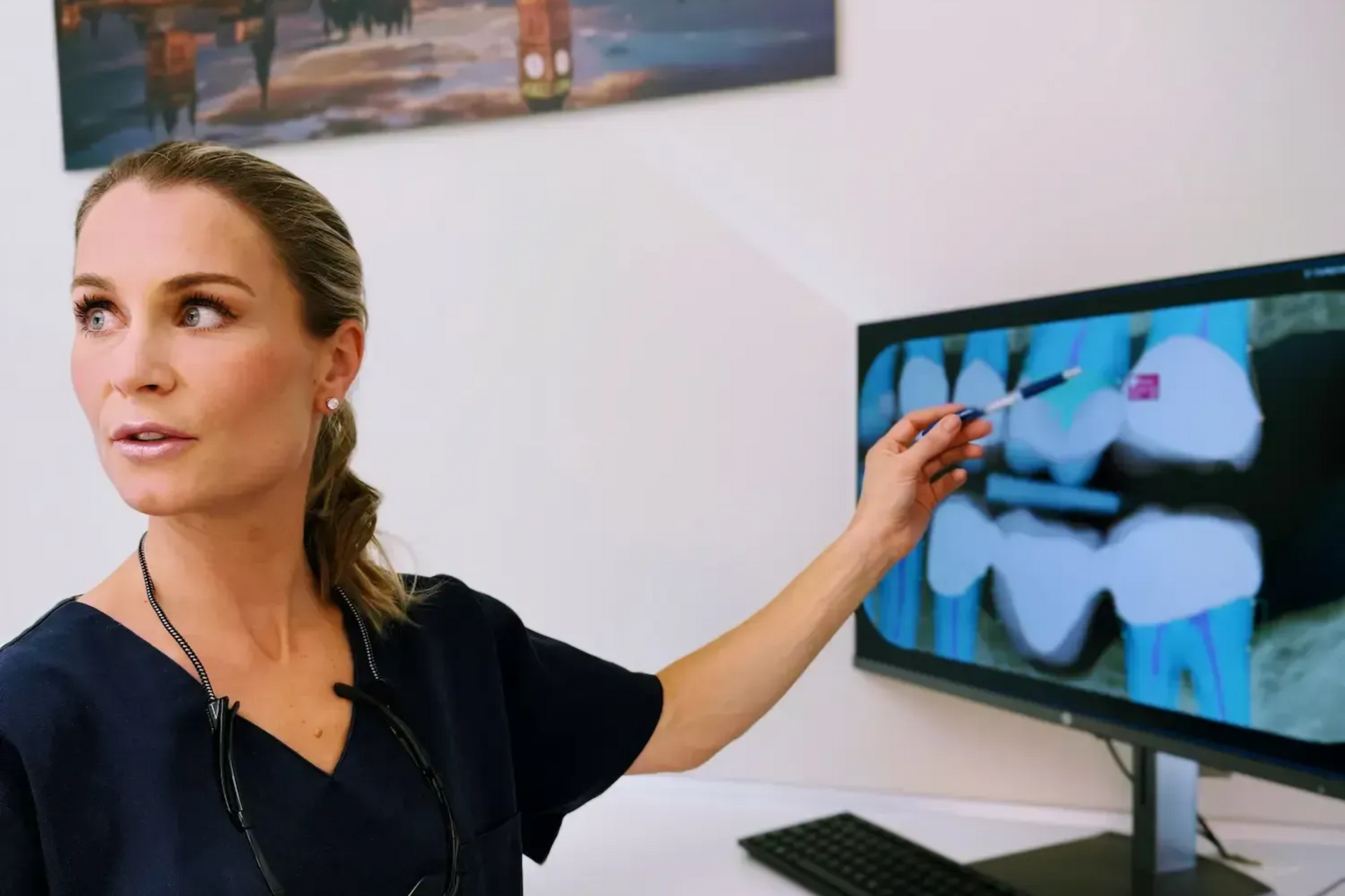 Tannlege peker på et røntgenbilde av tennene på en skjerm på et kontor.