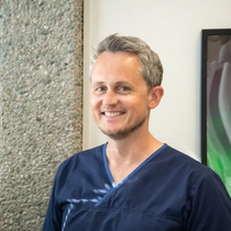 Mann i blå skrubber smiler; på kontor.