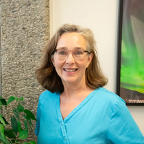 Tannlege Christian med briller og skjegg, iført blå skjorte og medisinsk maske, smiler til kameraet.