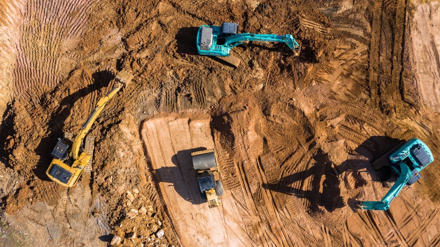Overhead view of an active construction site with several excavators moving earth.