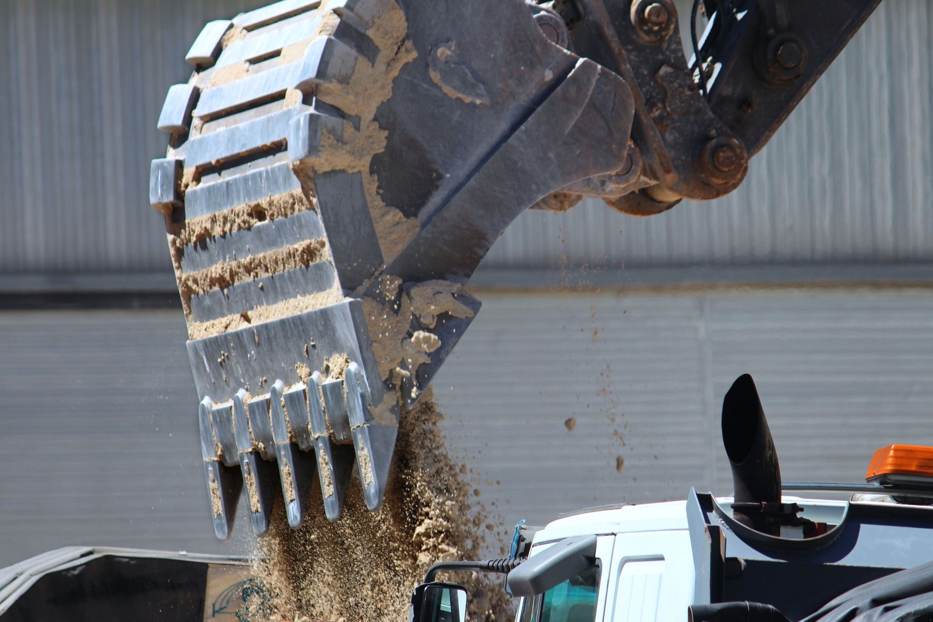 Excavator bucket dumping sand into a truck bed. Outdoors, daylight.