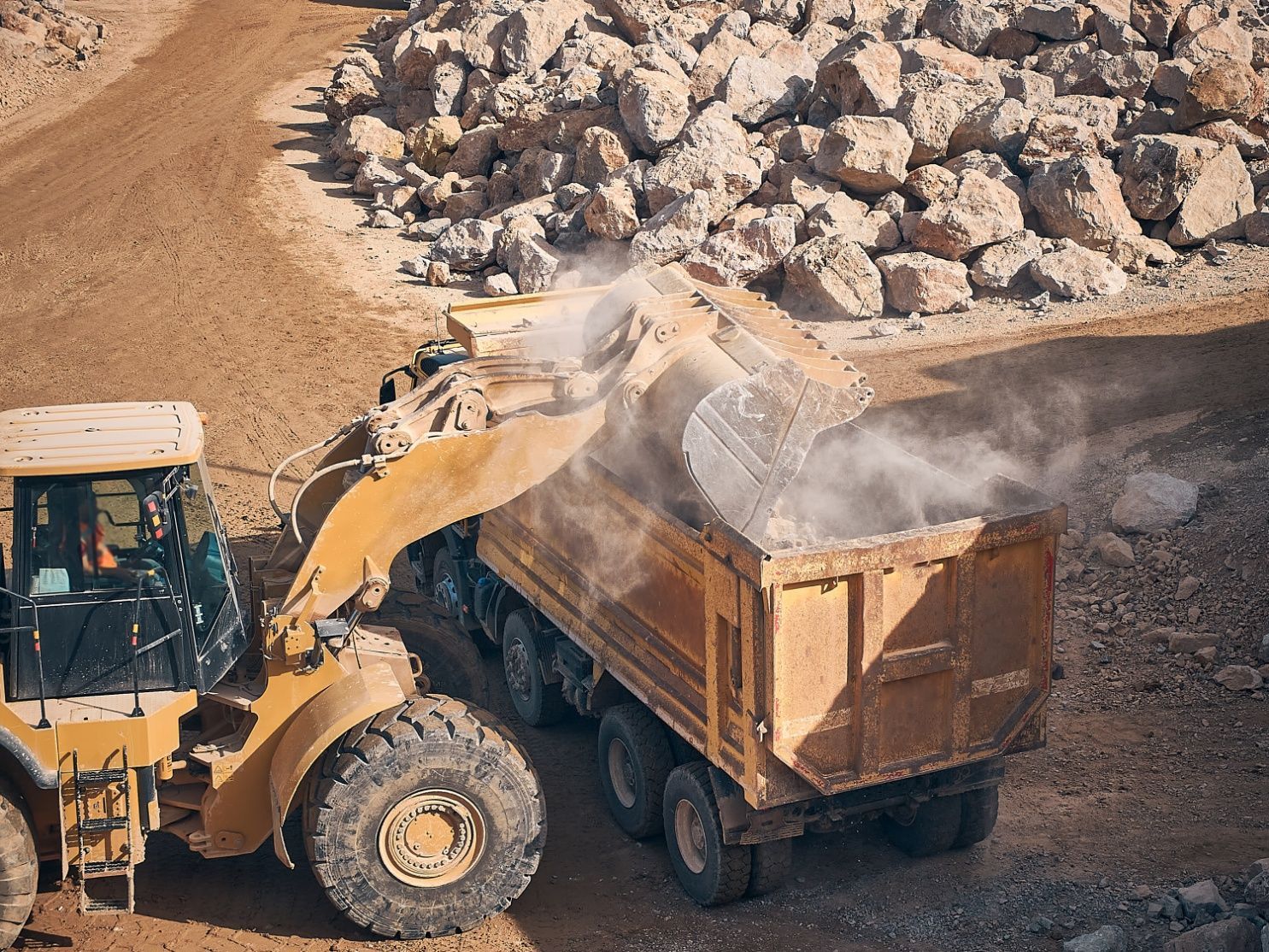 Yellow front-end loader filling a dump truck with rocks in a quarry.