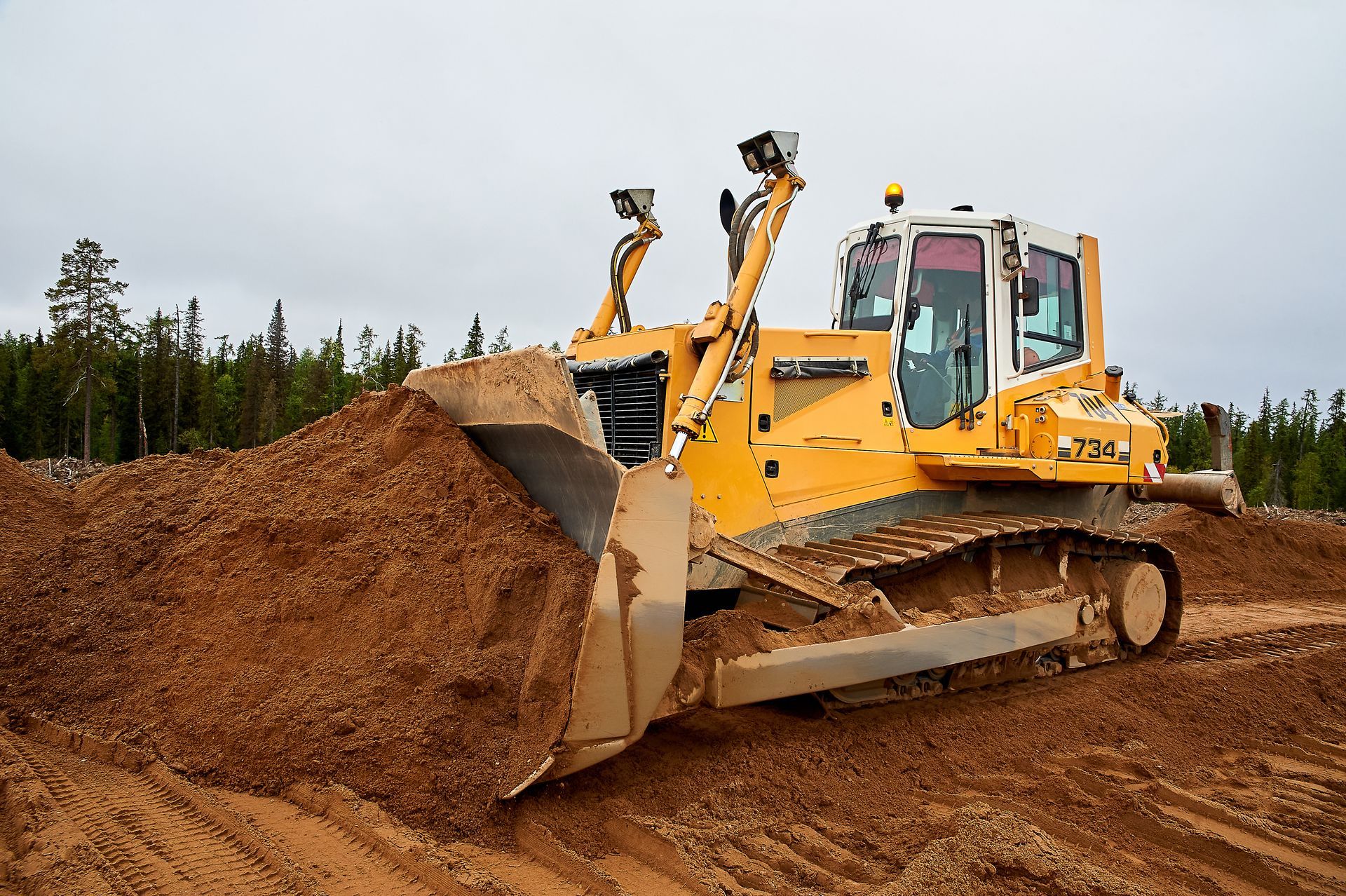 Overhead view of a yellow loader unloading a truck filled with trash at a facility.