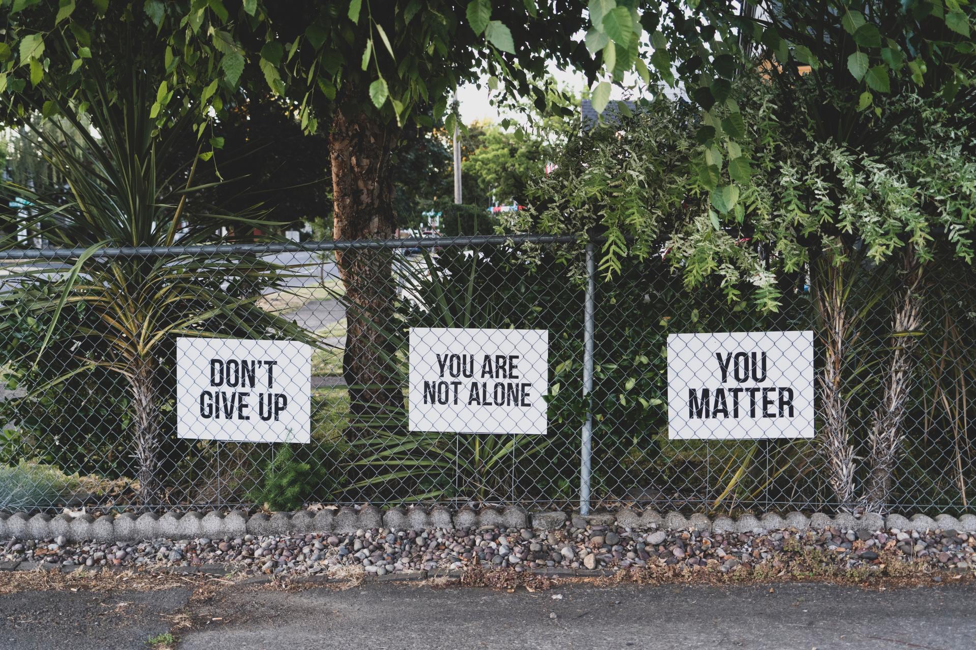 Three signs on a chain link fence saying do n't give up , you are not alone , and you matter.