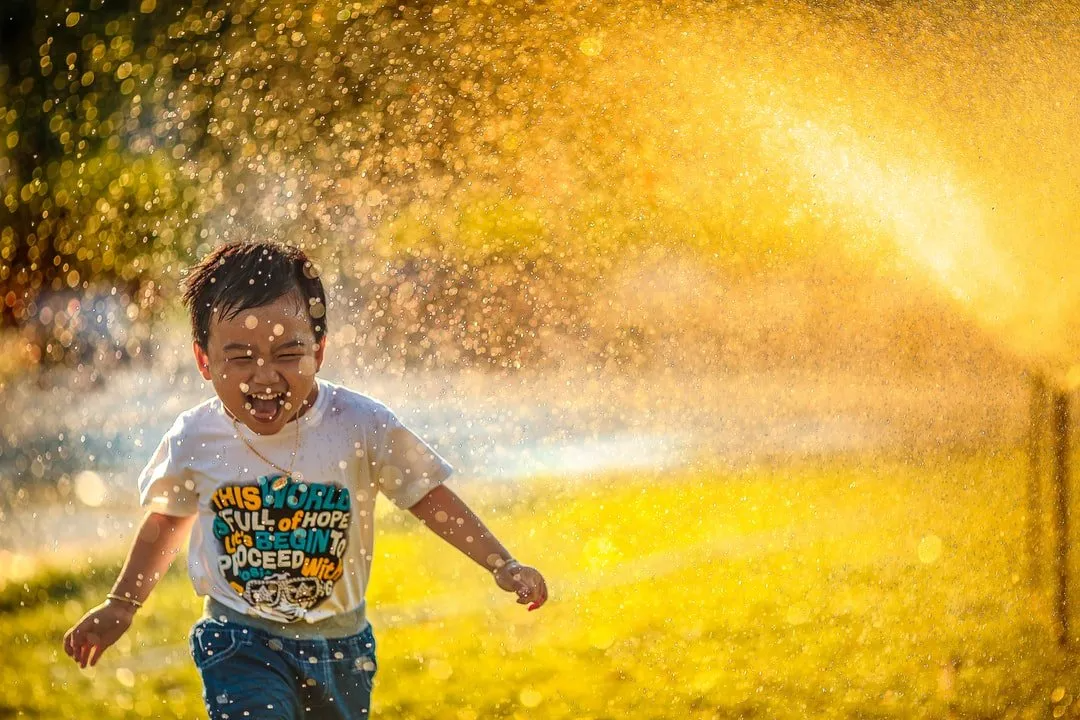 A young boy is running through a sprinkler in a park.