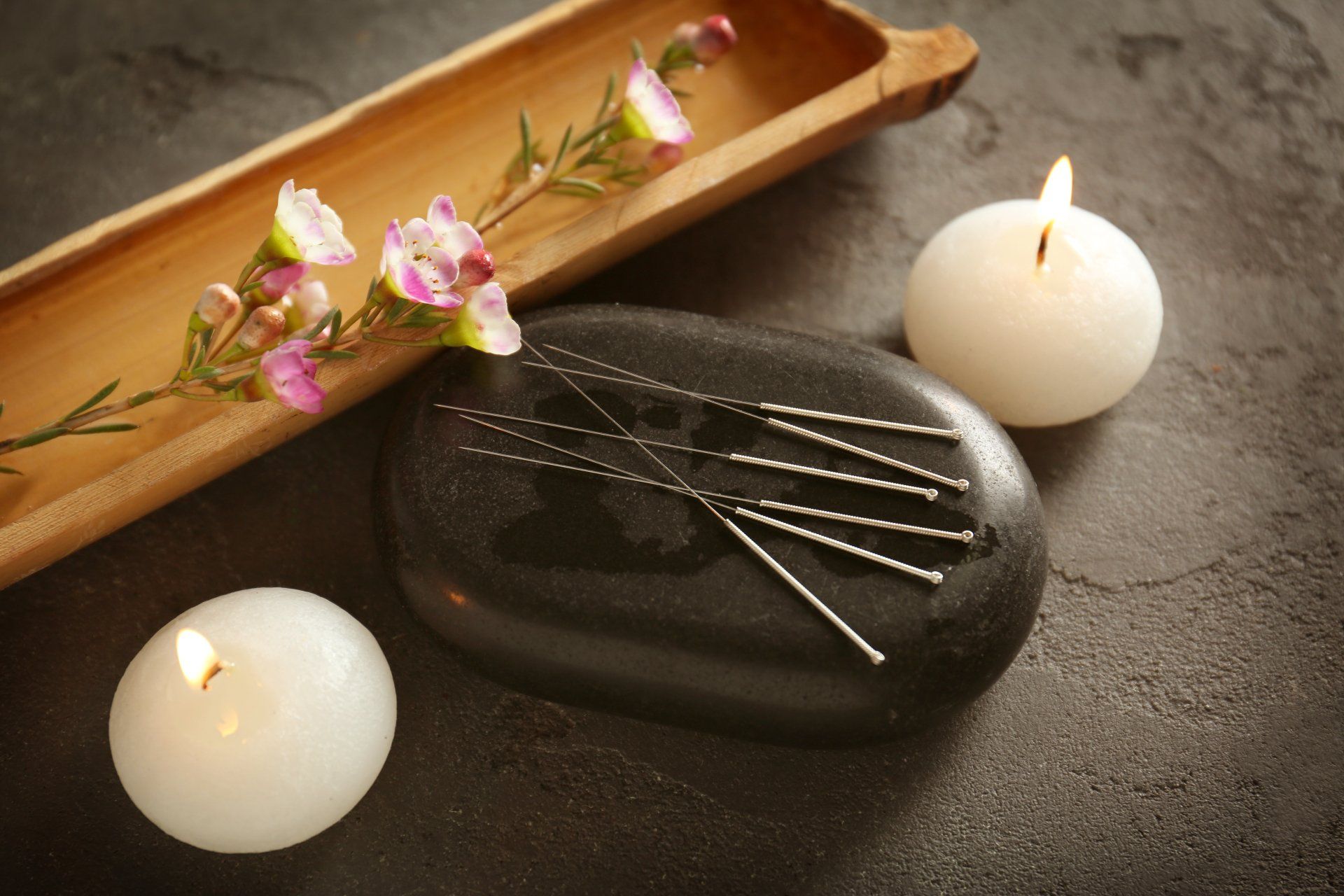 Acupuncture needles on a rock next to candles and flowers
