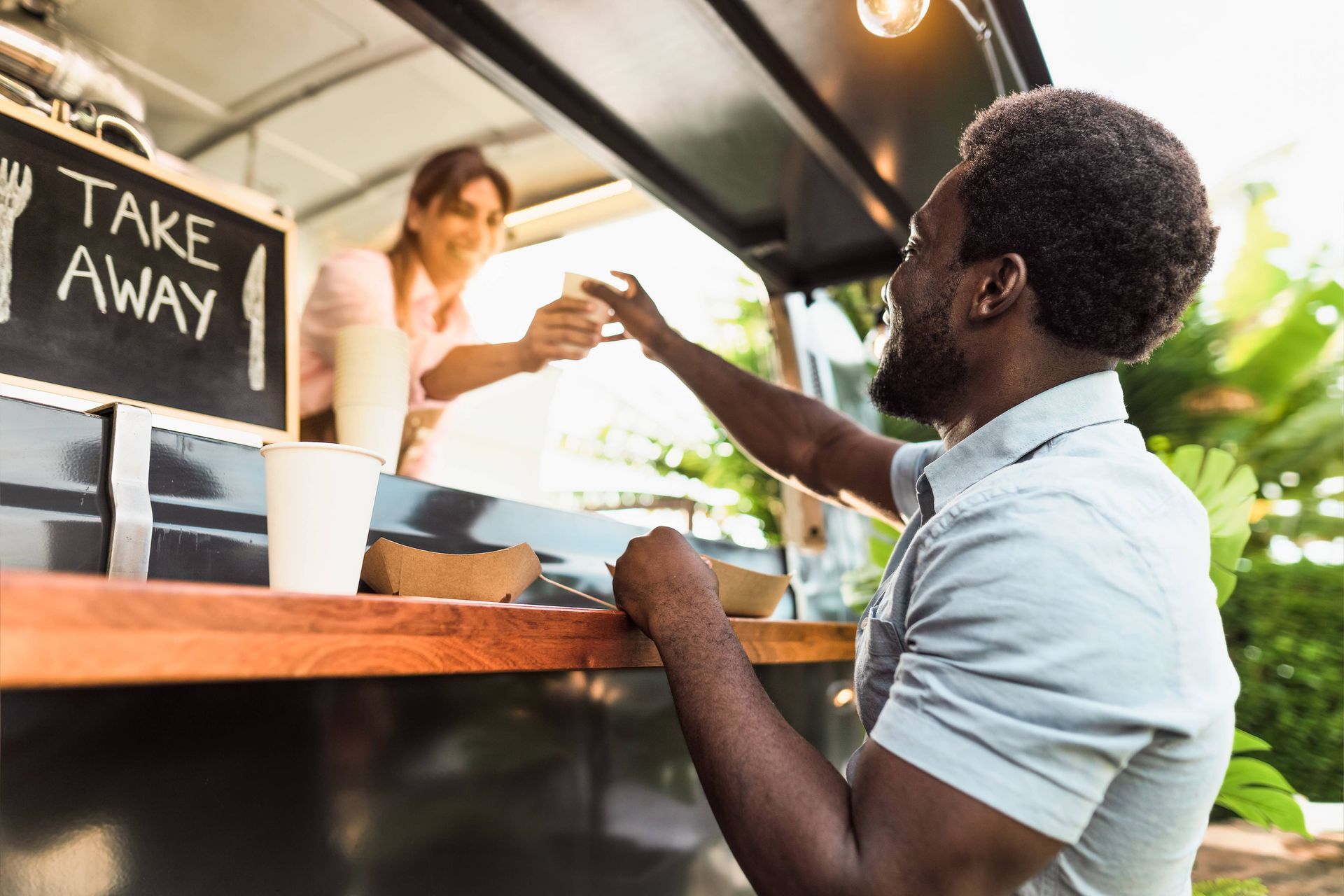 Man receiving food from a food truck window. Woman hands over food in a take-away container.