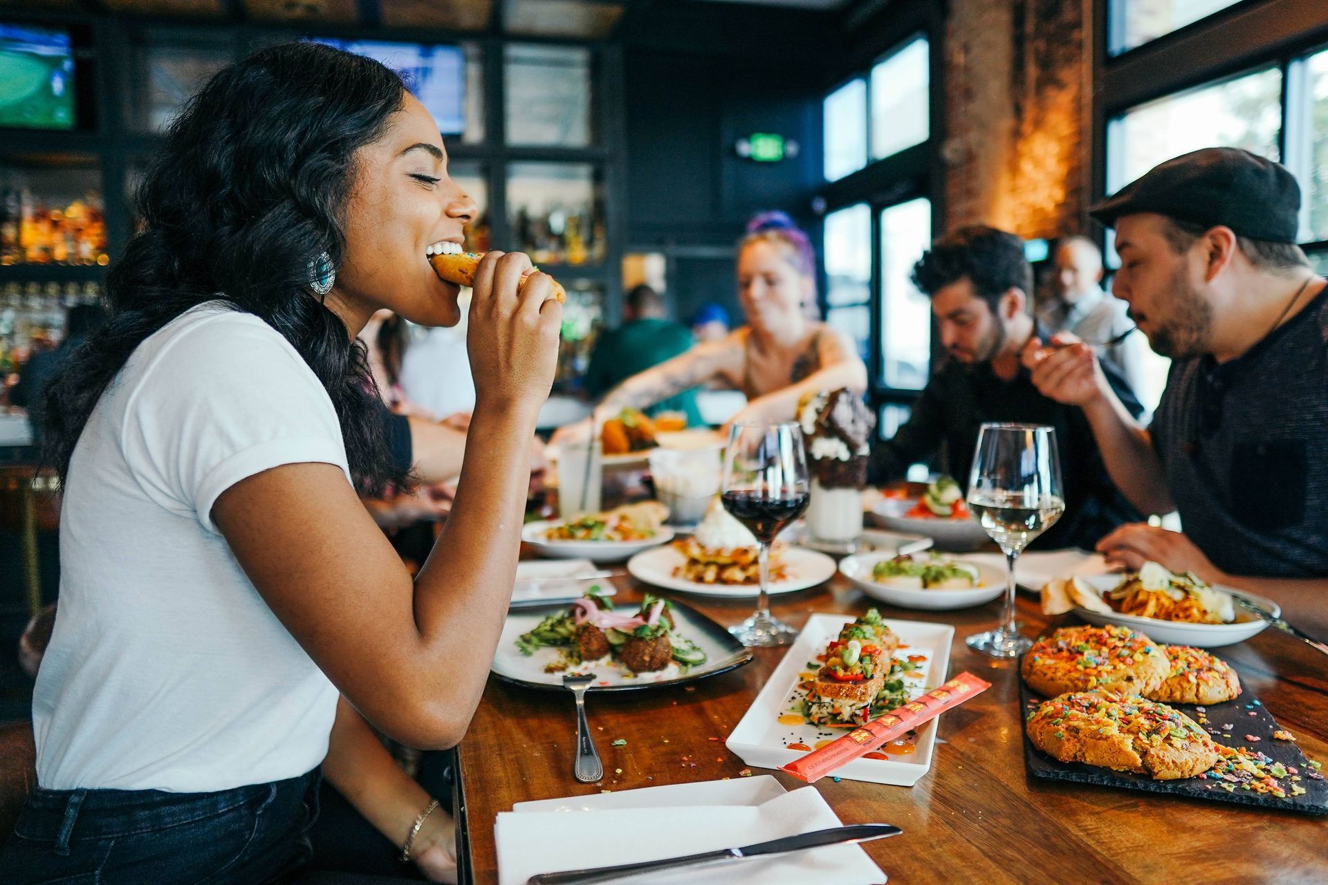 Group of people dining at a restaurant, enjoying various dishes and drinks. Woman eating food, smiling.