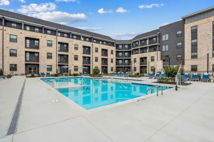 Swimming pool in a brick-paved courtyard, surrounded by trees and buildings with lounge chairs.