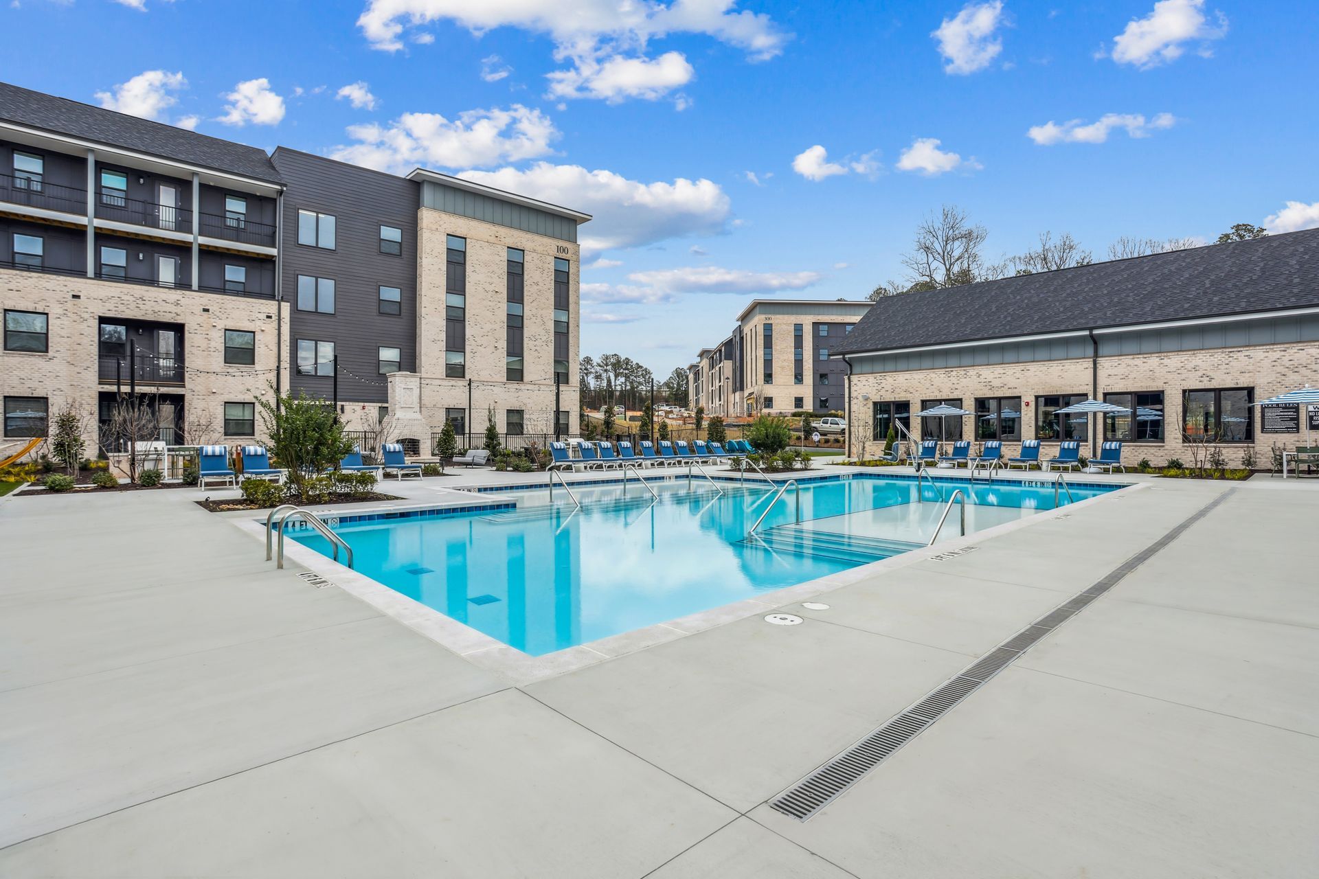 Swimming pool in a brick-paved courtyard, surrounded by trees and buildings with lounge chairs.