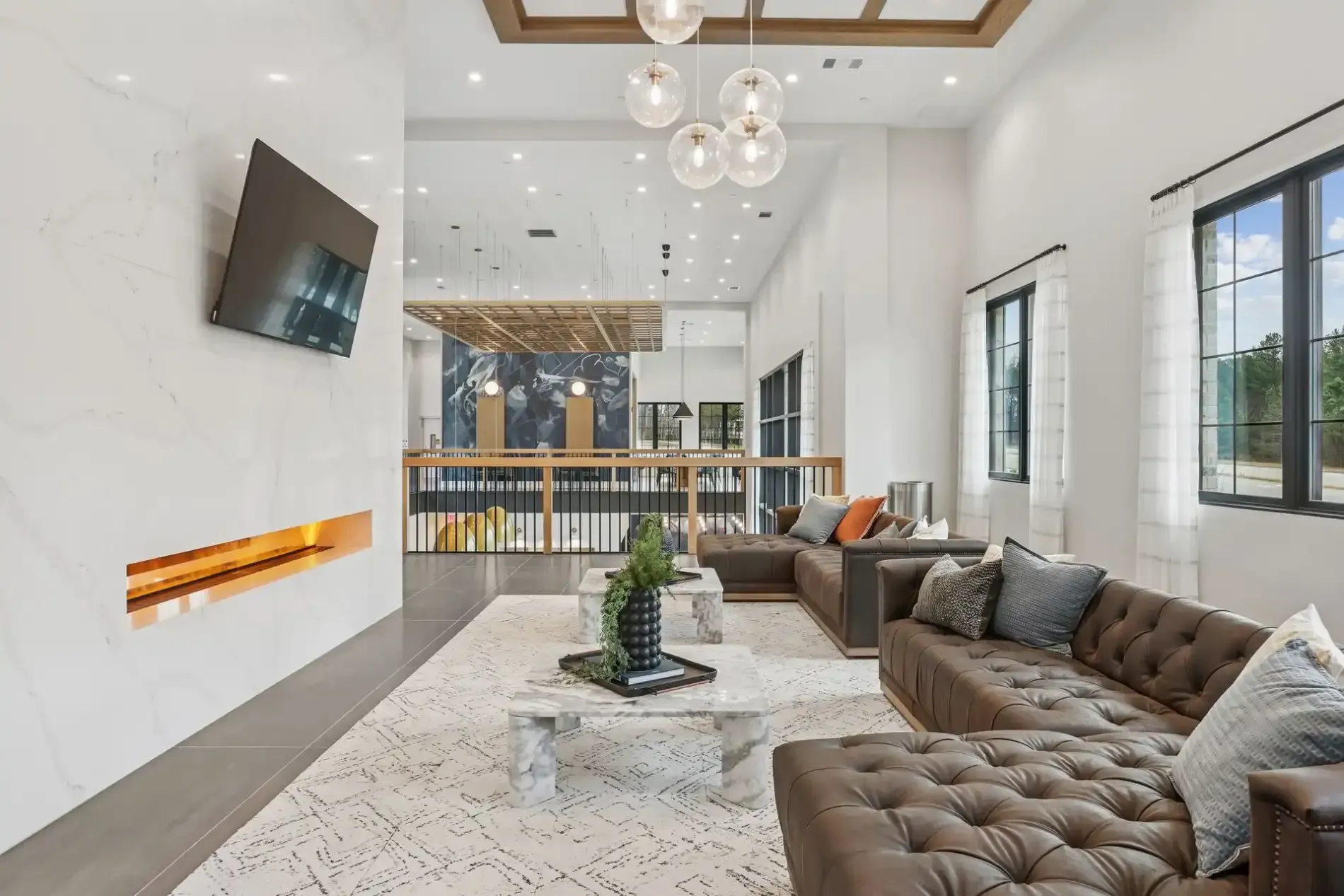 A modern, bright lounge with a marble fireplace, brown button-tufted sofas, a coffee table, and wood-paneled lighting.