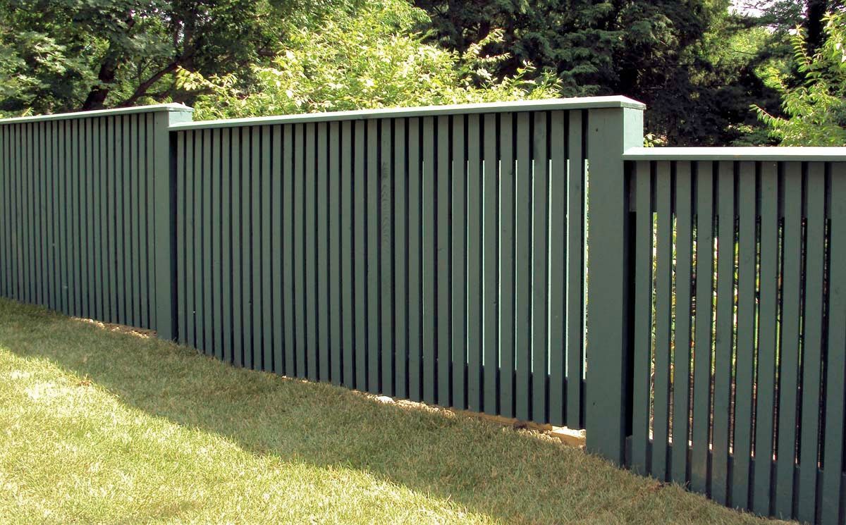 A green wooden fence surrounds a lush green yard.