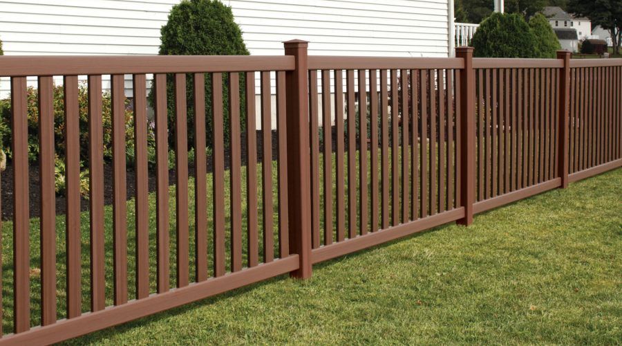 A wooden fence surrounds a lush green yard in front of a house.