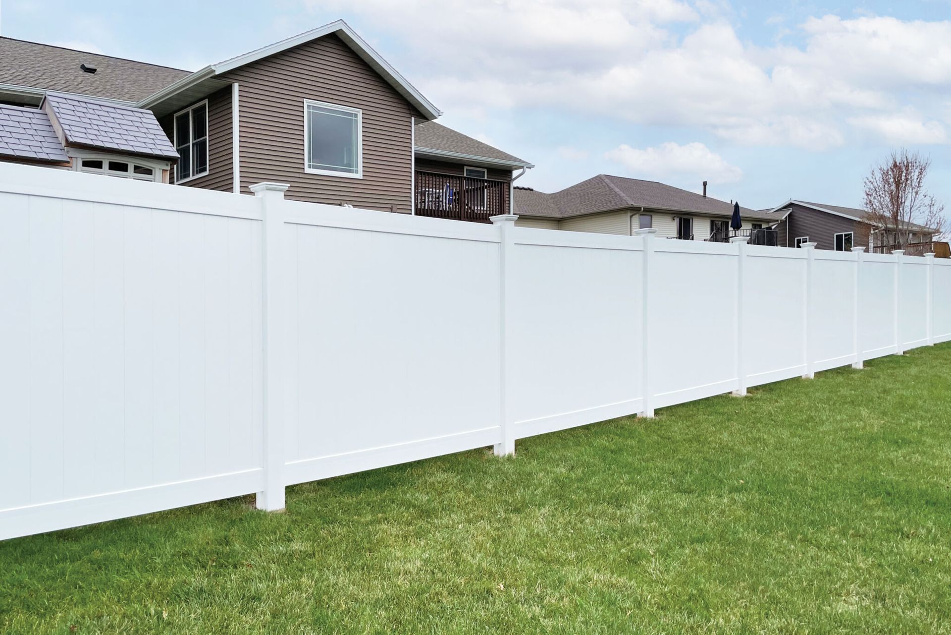 A white fence surrounds a lush green yard in front of a house.