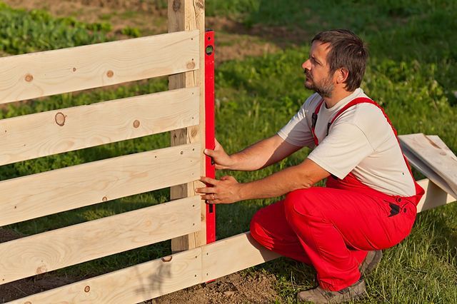 A man is measuring a wooden fence with a red level.