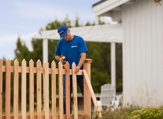 A man in a blue shirt is working on a wooden fence.