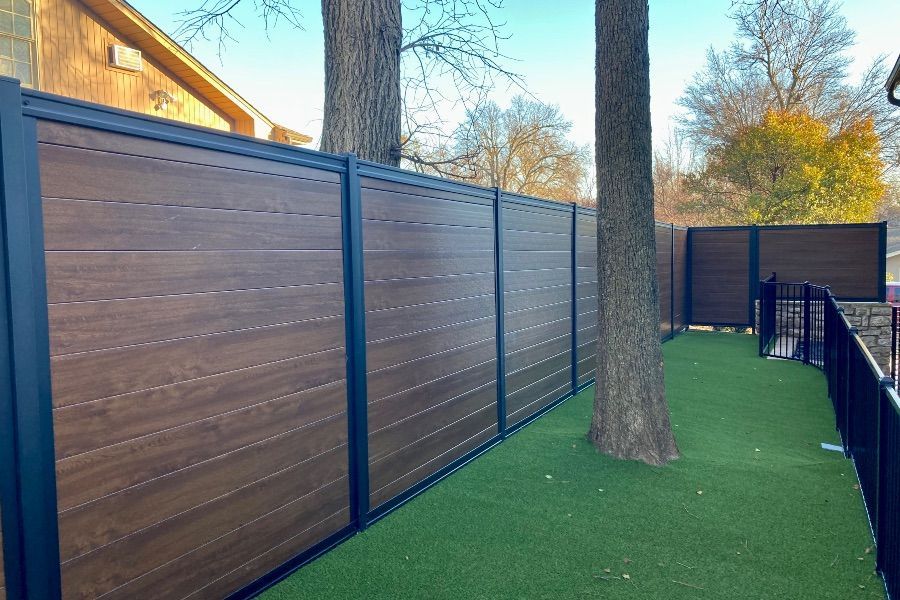 A wooden fence is surrounded by trees and grass in a backyard.