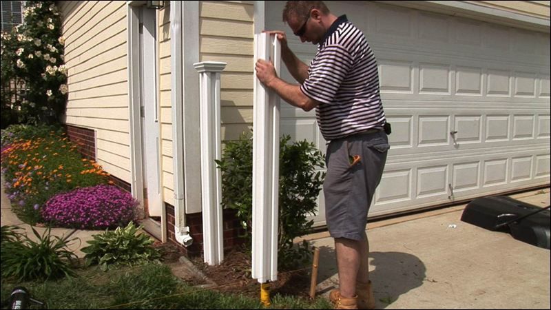 A man is installing a fence post in front of a garage door