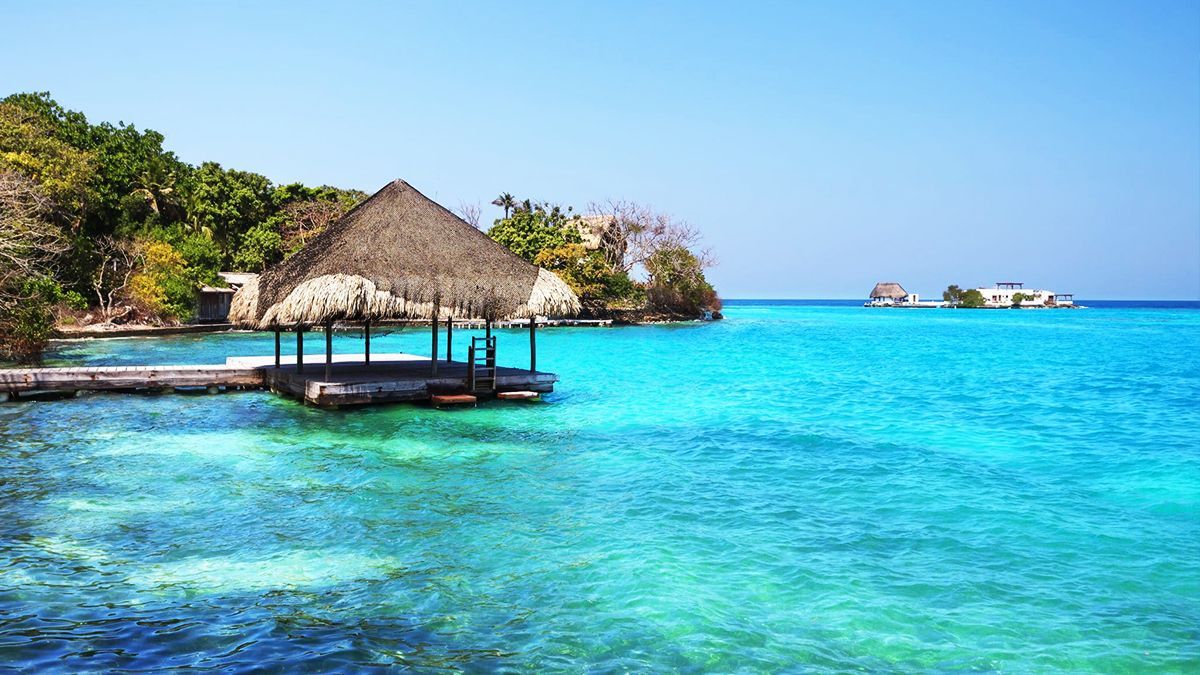 Muelle de madera con techo de paja sobre aguas turquesas cristalinas bajo un cielo azul.  | Mevak Agency