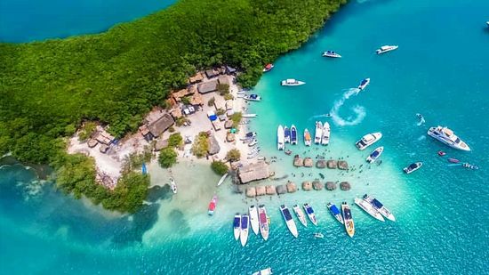 Isla con barcos en aguas turquesas y exuberante follaje verde | Mevak Agency