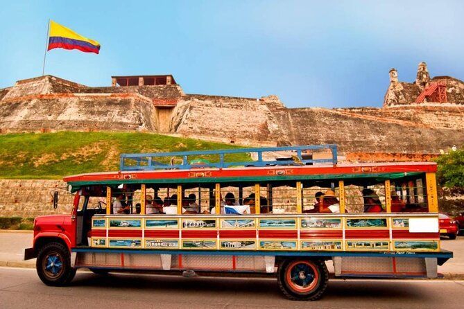 Colorido autobús abierto frente a una fortaleza con bandera colombiana.  | Mevak Agency