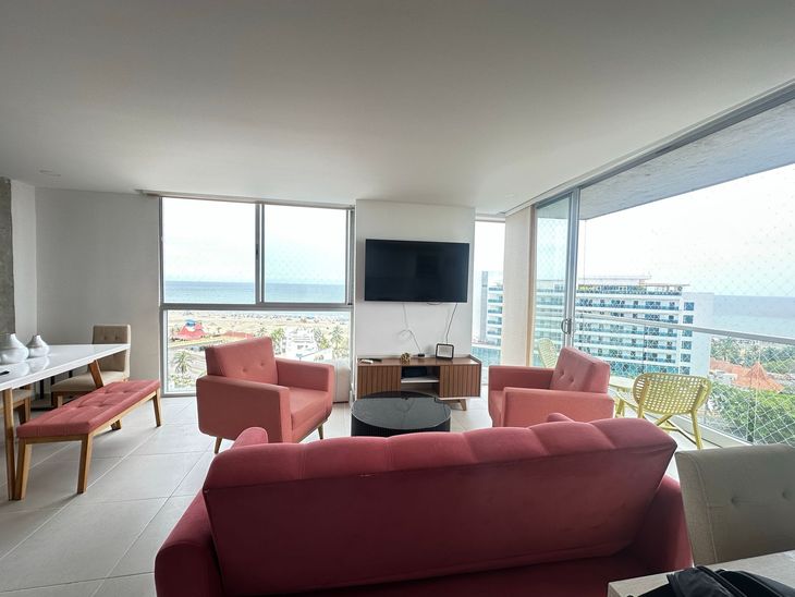 Moderna sala con muebles rosas, vista al mar y grandes ventanales.  | Mevak Agency