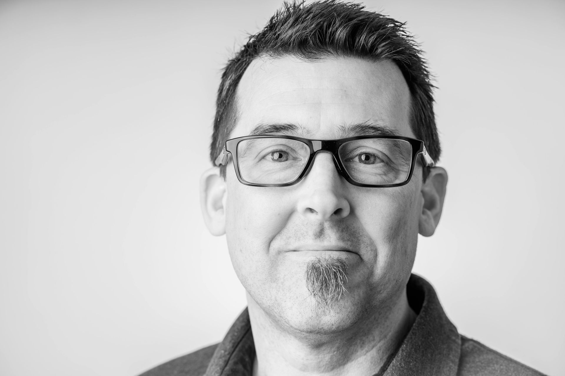 Hombre con esmoquin negro y pajarita, de pie frente a exuberantes plantas verdes. | Mevak Agency