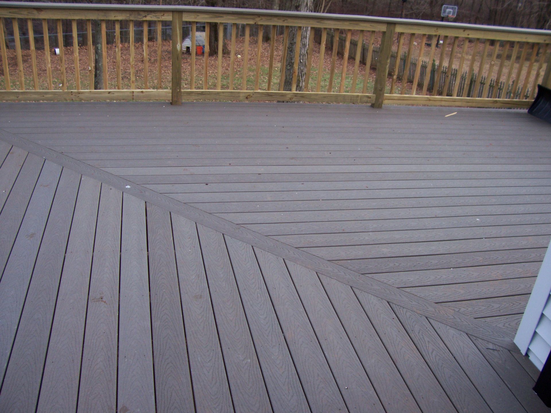 Wooden deck with diagonal design, railing, and fall foliage in the background.