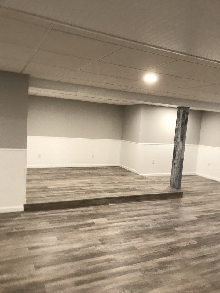 Empty finished basement with laminate flooring, white and gray walls, and a support beam.