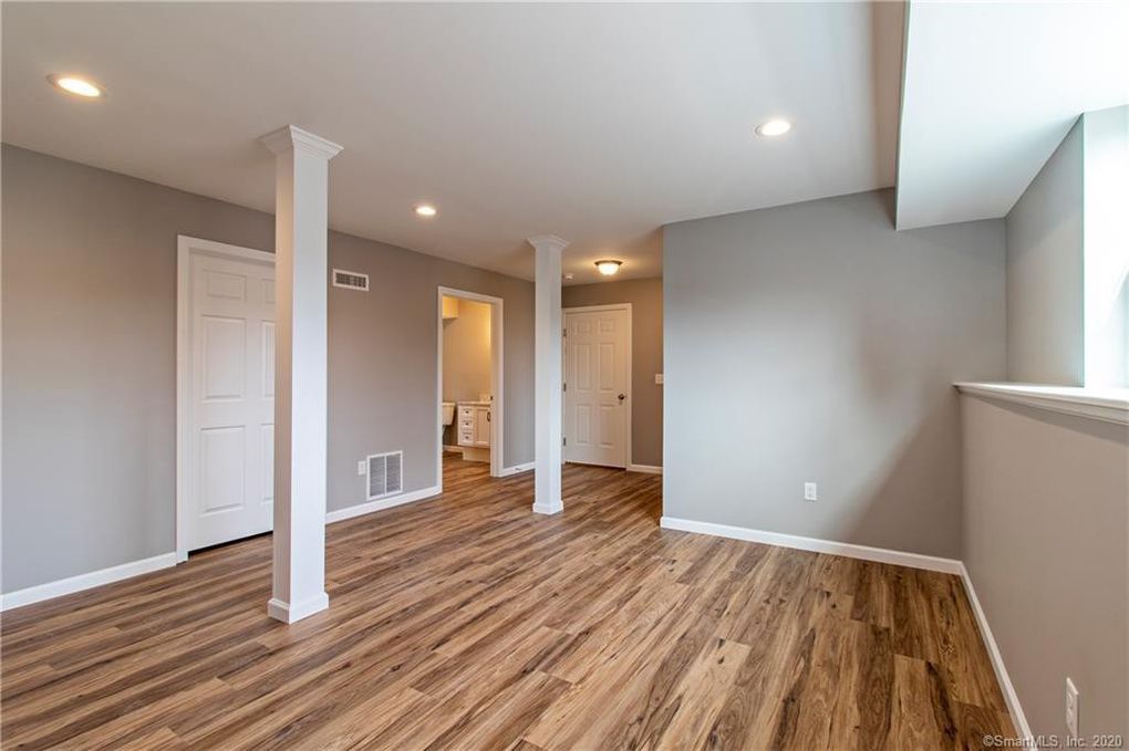Finished basement with wood-look flooring, gray walls, white columns, and recessed lighting.