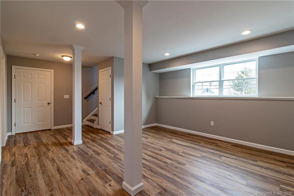 Basement room with gray walls, wood flooring, support beams, and a small window.