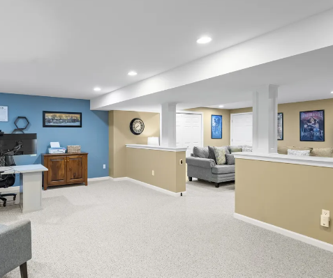 Spacious basement with light carpet, blue and beige walls, and a sitting area with a gray couch.
