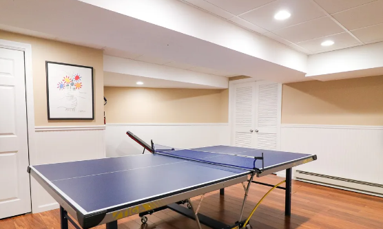 Ping pong table in a finished basement with wainscoting and artwork on the wall.