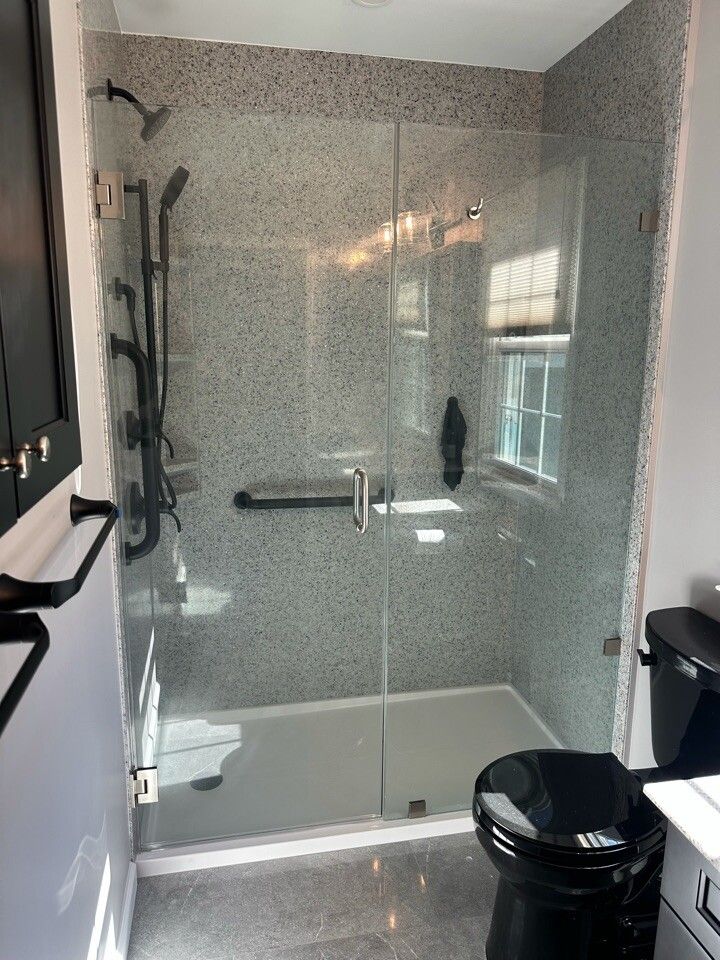 Bathroom with glass shower, speckled wall tile, black fixtures, and a black toilet.
